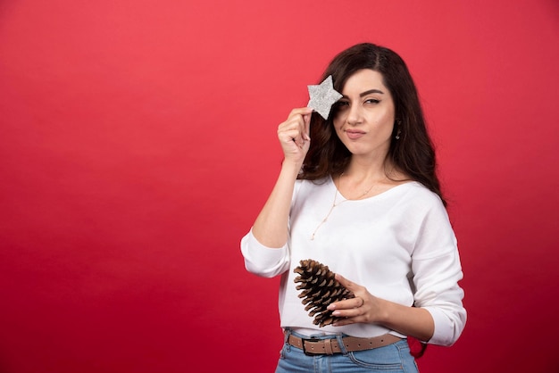 Jeune femme posant avec une grosse pomme de pin de Noël et une étoile sur fond rouge. photo de haute qualité