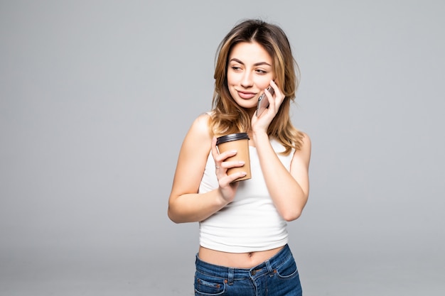 Jeune femme posant isolé sur mur gris mur parler par téléphone portable, boire du café.