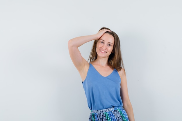 Jeune femme posant avec la main sur la tête en maillot, jupe et à la recherche de mignon. vue de face.