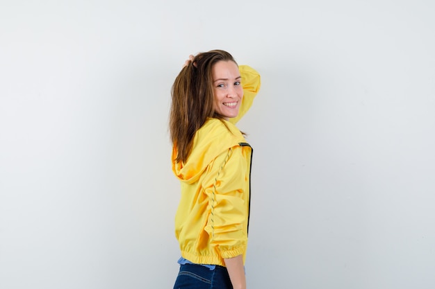 Jeune femme posant avec la main sur la tête en veste jaune et à la séduisante.