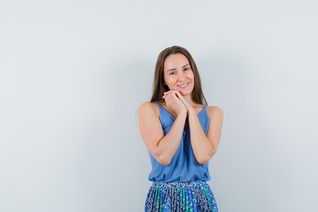 Jeune femme posant avec les mains combinées sur la poitrine en chemisier, jupe et à la recherche d'émotions. vue de face.