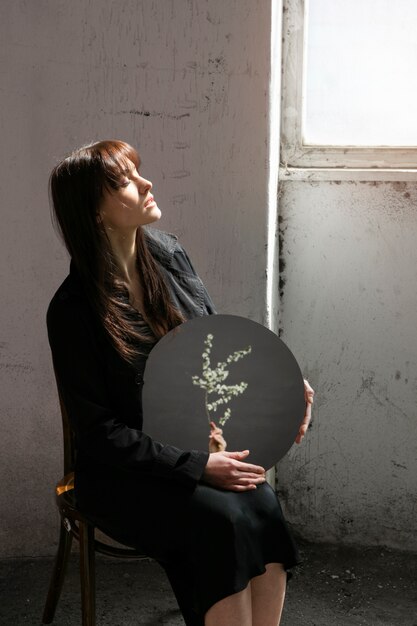 Jeune femme posant avec miroir à l'intérieur du bâtiment à côté de la fenêtre