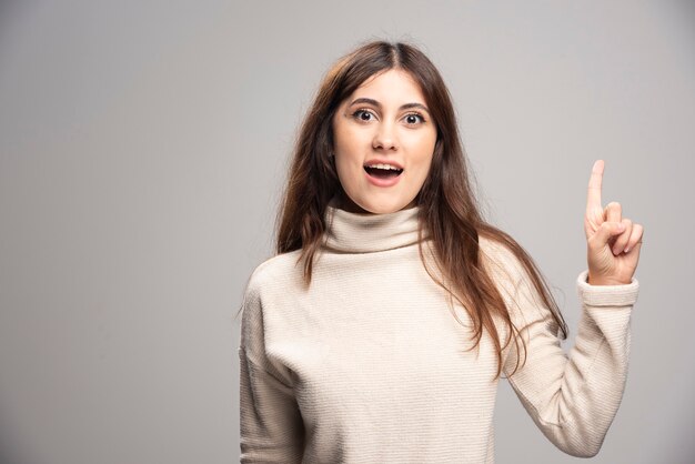 Une jeune femme posant et pointant l'index de côté vers le haut.