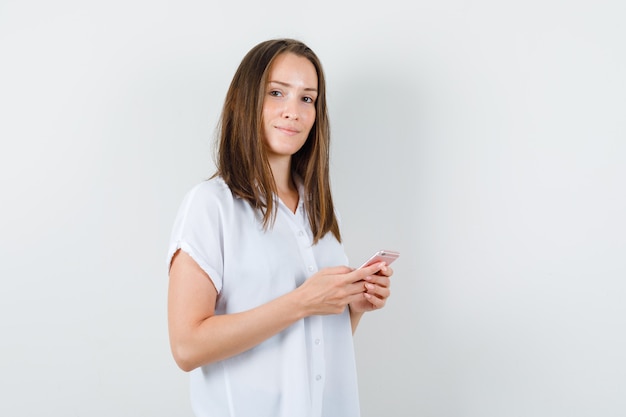 Jeune femme posant avec téléphone en chemisier blanc et à la recherche de calme.