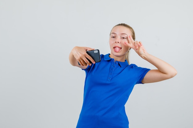 Jeune femme posant tout en prenant selfie en t-shirt bleu et à la folle