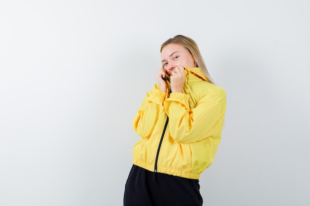 Jeune femme posant tout en tenant le col de sa veste en veste jaune, pantalon et à la vue de face, paisible.