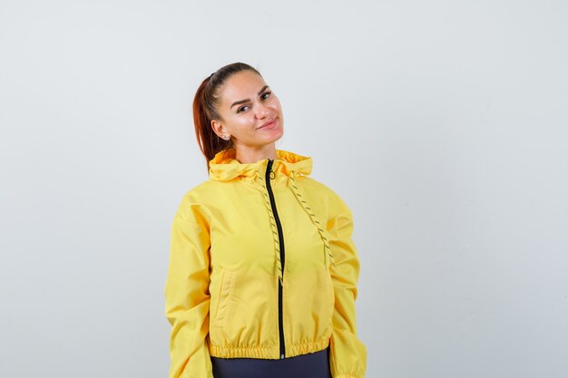 Jeune femme posant en veste jaune et semblant ravie. vue de face.