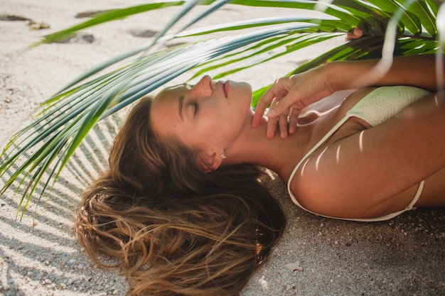 Photo gratuite jeune femme, pose, sur, plage sable, sous, feuille palmier