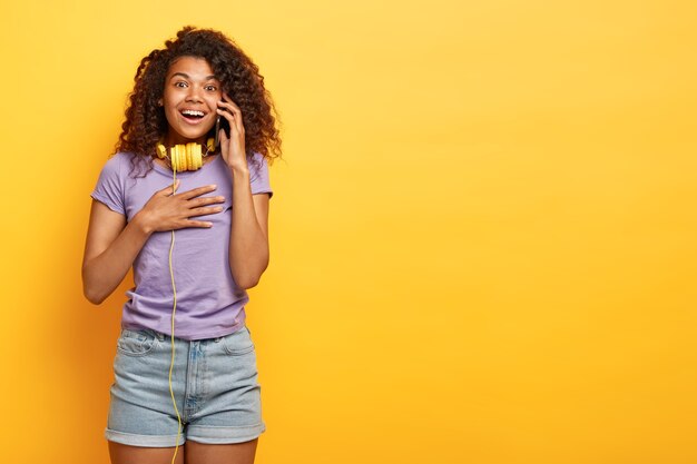 Jeune femme positive avec une coiffure afro posant contre le mur jaune