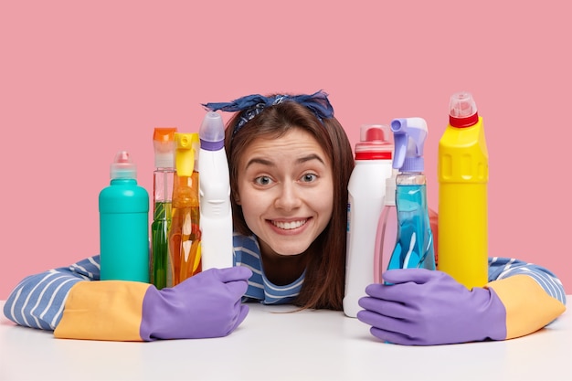 Jeune femme positive avec une expression ravie, sourire à pleines dents, embrasse les détergents chimiques, regarde avec plaisir