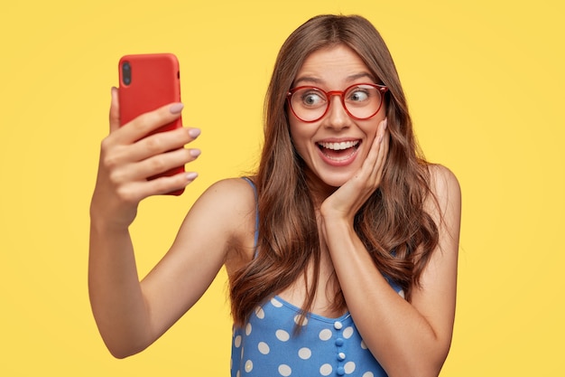 jeune femme positive avec des lunettes posant contre le mur jaune