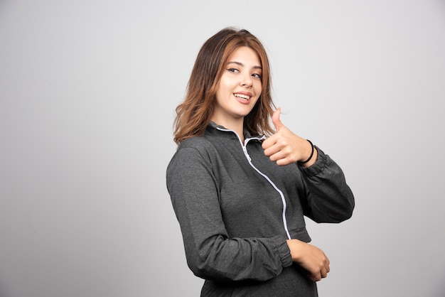 Jeune femme avec le pouce contre le mur gris.