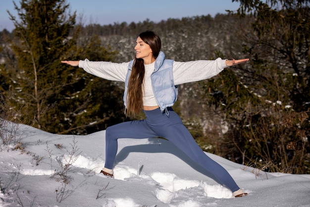 Photo gratuite jeune femme pratiquant le yoga à l'extérieur pendant l'hiver entouré d'arbres