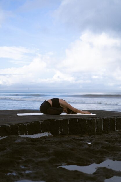 Jeune femme pratique le yoga sur une belle plage au lever du soleil. Ciel bleu, océan, vagues, proximité avec la nature, unité avec la nature.