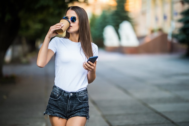 Jeune femme prenant une pause-café et utilisant un smartphone dans la rue