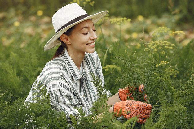 Jeune femme prenant soin des plantes. Brunette dans un chapeau et des gants.