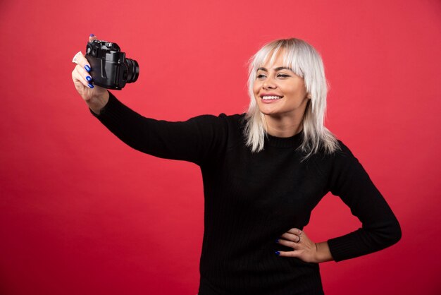 Jeune femme à prendre des photos avec un appareil photo sur fond rouge. Photo de haute qualité