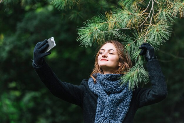 Jeune femme, prendre, selfie, sur, smartphone, près, brindille conifère