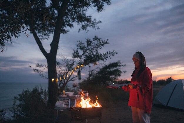 Jeune femme préparant des aliments sur le grill au bord de la mer