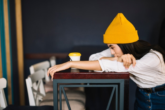 Photo gratuite jeune femme près de tasse de boisson se penchant à table