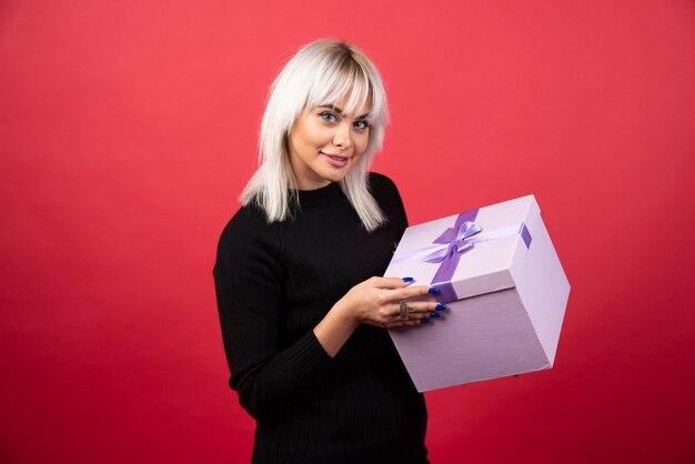 Jeune femme avec présent sur fond rouge. Photo de haute qualité