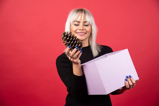 Jeune femme avec présent tenant une grosse pomme de pin sur fond rouge. Photo de haute qualité