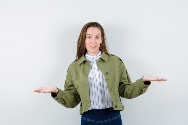 Jeune femme présentant ou comparant quelque chose en chemise, veste et semblant confiante. vue de face.