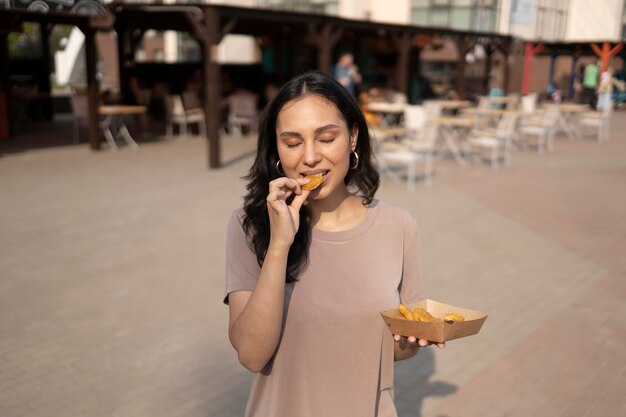 Photo gratuite jeune femme profitant de la nourriture de rue à l'extérieur