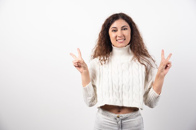 Jeune femme en pull blanc aux cheveux bouclés posant. Photo de haute qualité