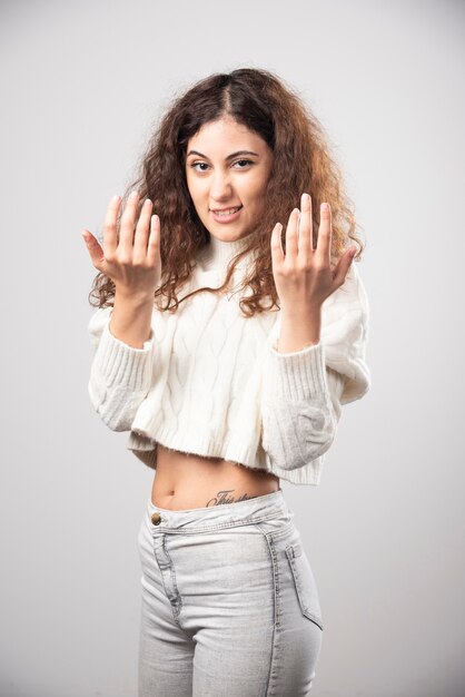 Jeune femme en pull blanc debout sur un mur blanc. Photo de haute qualité