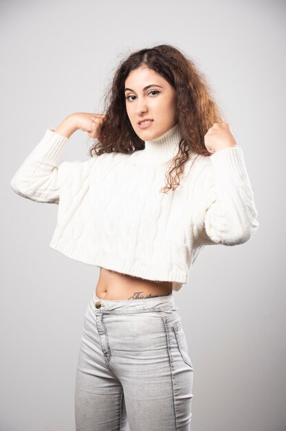 Jeune femme en pull blanc debout sur un mur blanc. Photo de haute qualité