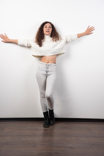 Photo gratuite jeune femme en pull blanc debout sur un mur blanc. photo de haute qualité