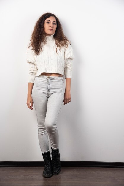 Jeune femme en pull blanc debout sur un mur blanc. Photo de haute qualité