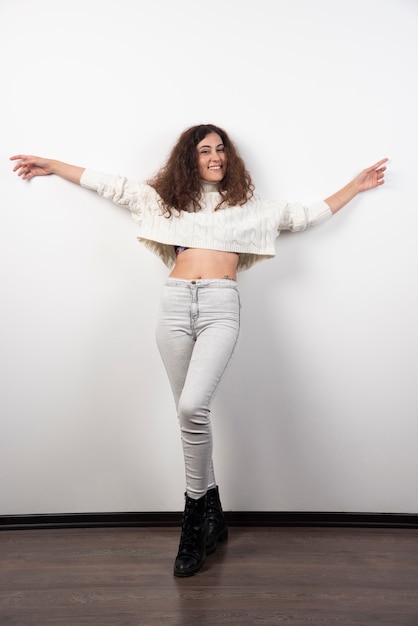 Photo gratuite jeune femme en pull blanc debout sur un mur blanc. photo de haute qualité