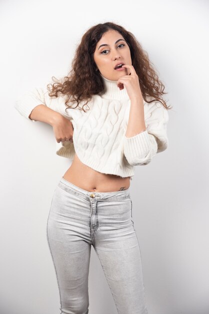 Jeune femme en pull blanc debout sur un mur blanc. Photo de haute qualité