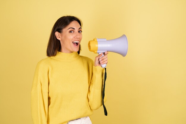 Jeune femme en pull chaud jaune avec haut-parleur mégaphone excité et criant