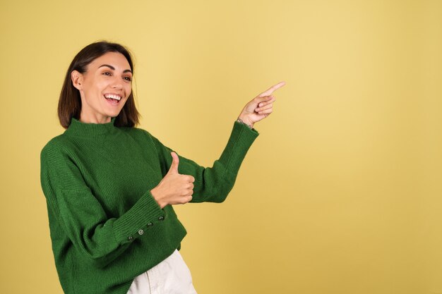 Jeune femme en pull chaud vert pointant les doigts vers la droite