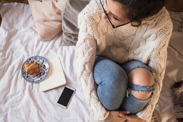 Jeune femme en pull et jeans assis sur un lit