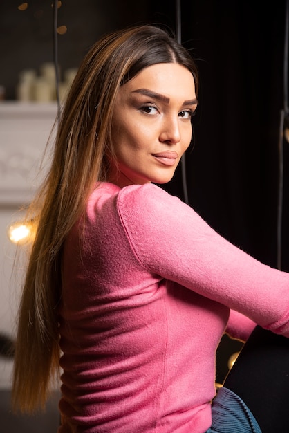 Photo gratuite une jeune femme en pull rose assise près des lampes.