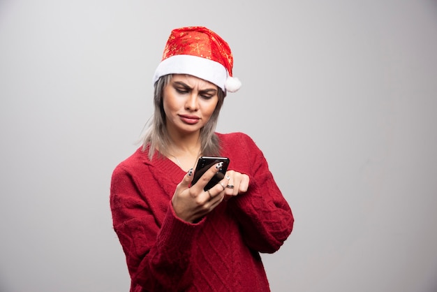 Jeune femme en pull rouge regardant intensément le téléphone portable sur fond gris.