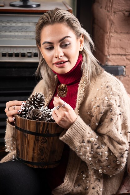 Jeune femme en pull rouge tenant un panier en bois plein de pommes de pin