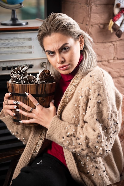 Jeune femme en pull rouge tenant un panier en bois plein de pommes de pin