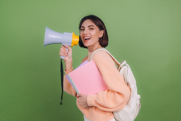 Jeune femme en pull et sac à dos pêche occasionnel isolé sur mur de couleur olive verte