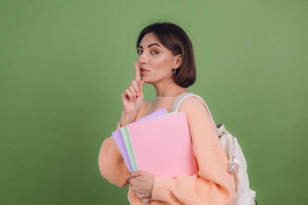 Jeune femme en pull et sac à dos pêche occasionnel isolé sur mur de couleur olive verte