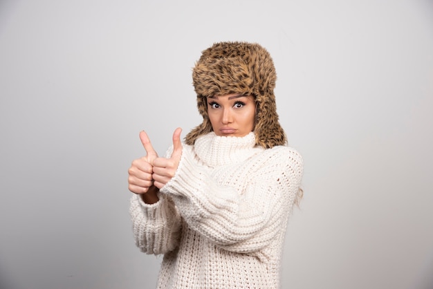 Jeune femme en pull tricoté blanc donnant les pouces vers le haut.