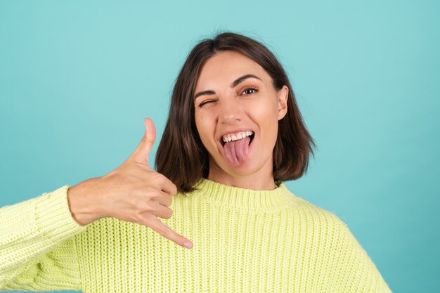 Jeune femme en pull vert clair souriant montre le geste du téléphone