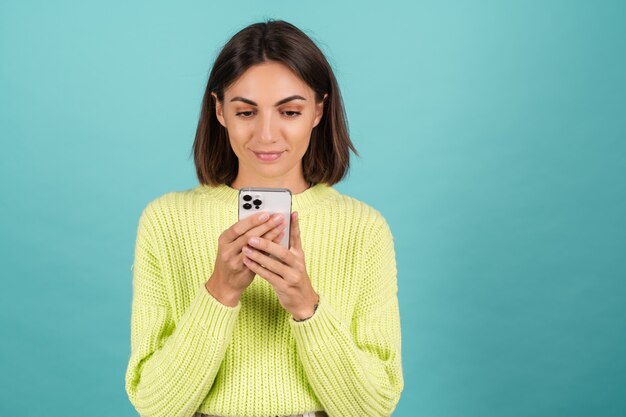 Jeune femme en pull vert clair avec un téléphone portable avec un message de saisie de sourire