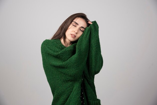 Jeune femme en pull vert dormant sur gris.