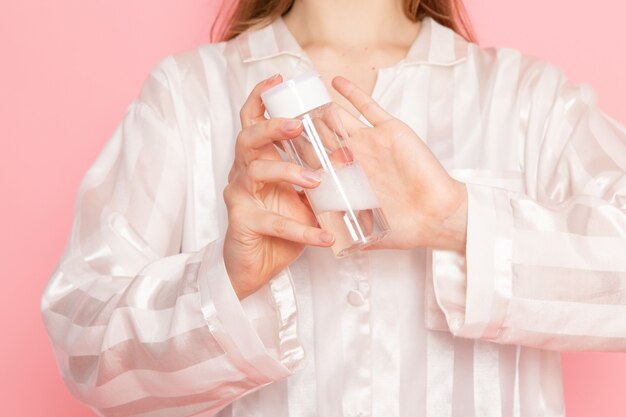 Jeune femme en pyjama et masque de sommeil à l'aide de spray de maquillage sur rose