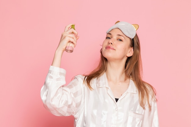 Jeune femme en pyjama et masque de sommeil à l'aide de spray sur rose